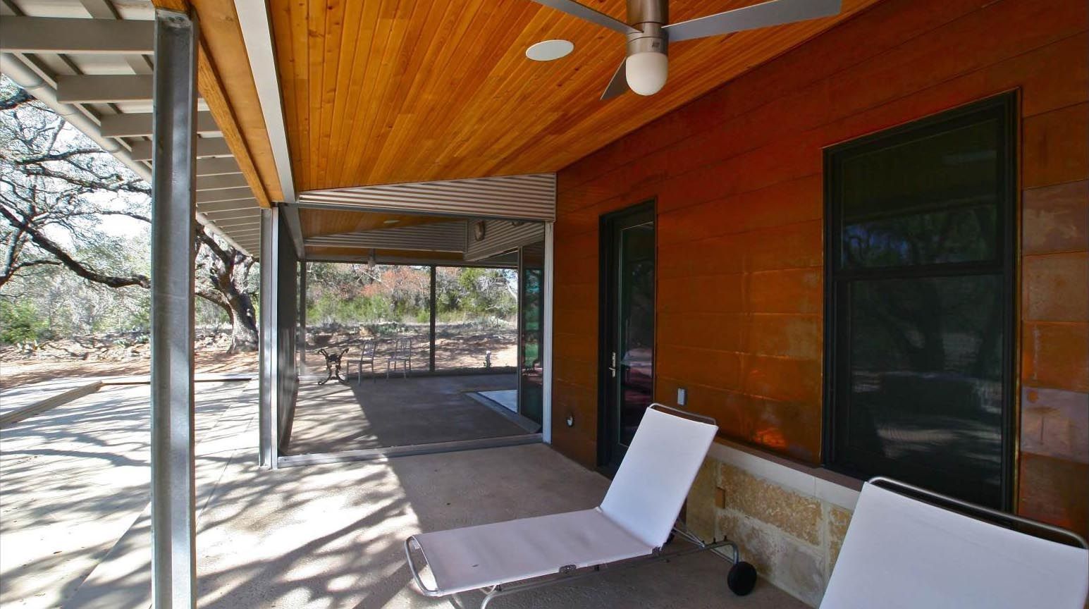 Outdoor patio with wood ceiling, metal supports, and two white chairs.