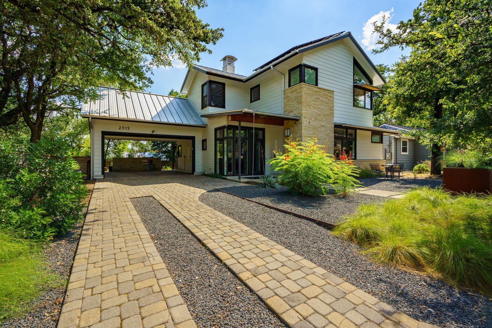 Two-story modern home with a paver driveway, carport, and landscaped front yard.