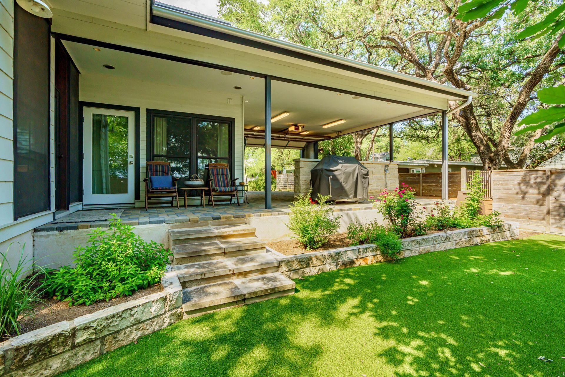 Covered patio with grill, steps, and green lawn.