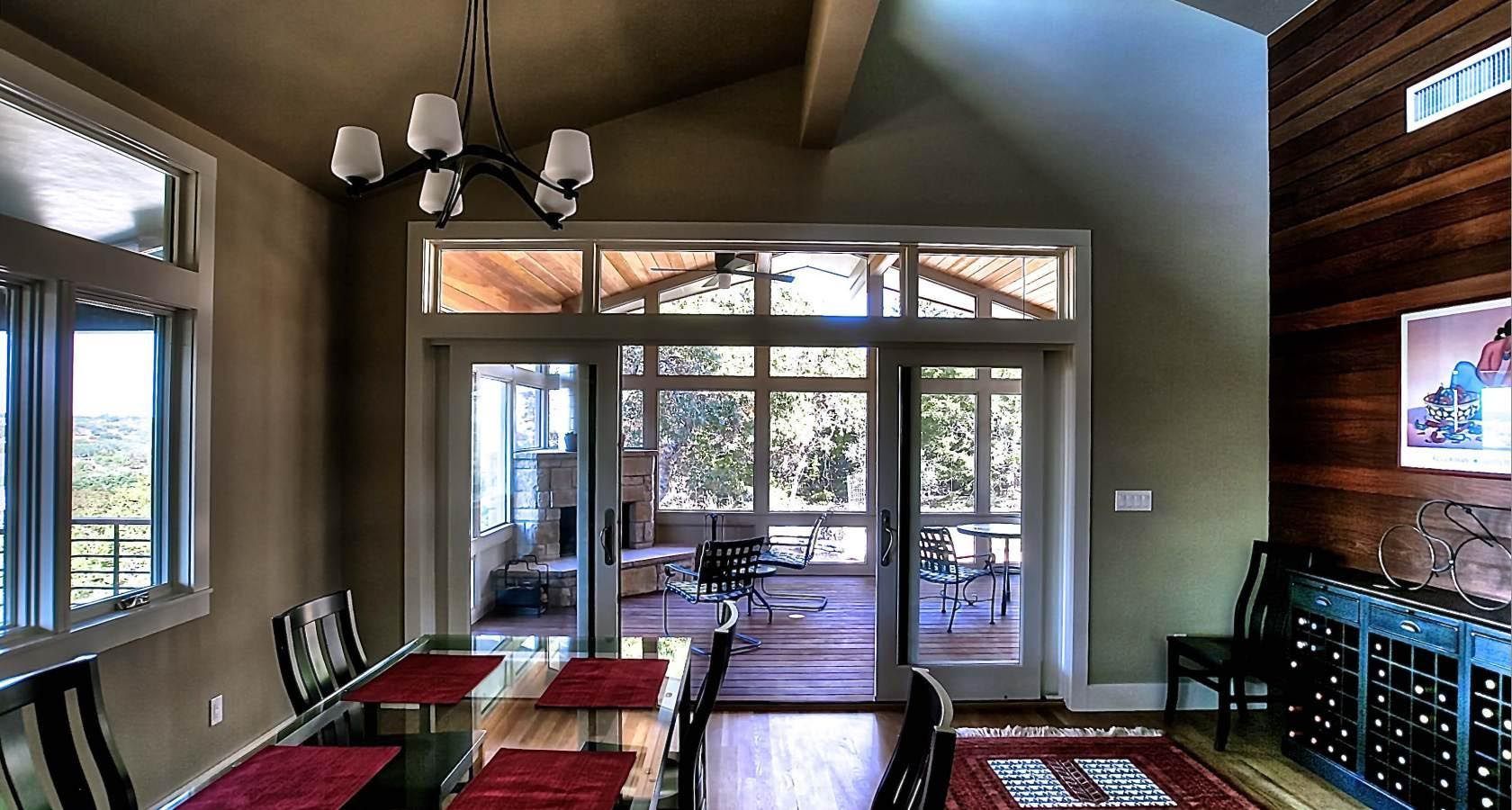 Dining room with a table, chairs, and doors leading to a porch. Green walls and a wine rack are visible.