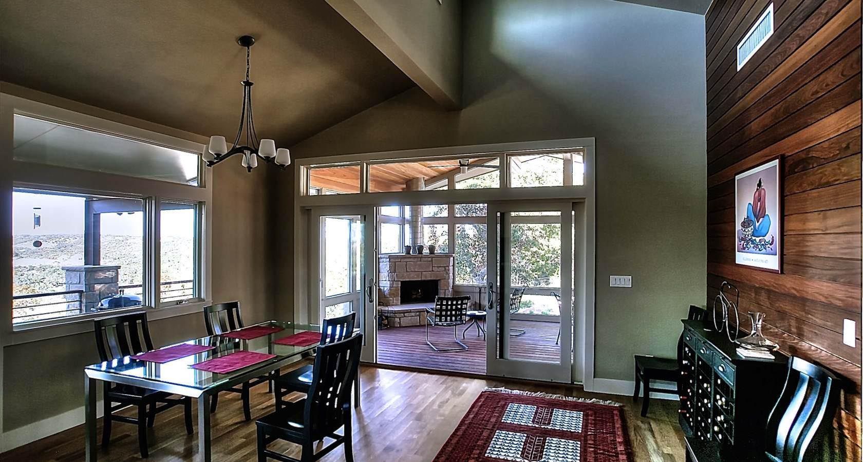 Dining room with table, chairs, windows, and view to a living space with fireplace and wood-paneled wall.
