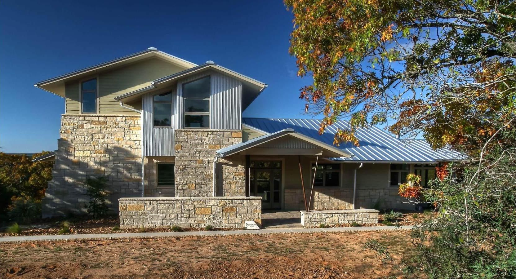 Two-story house with stone and metal facade under a clear blue sky.