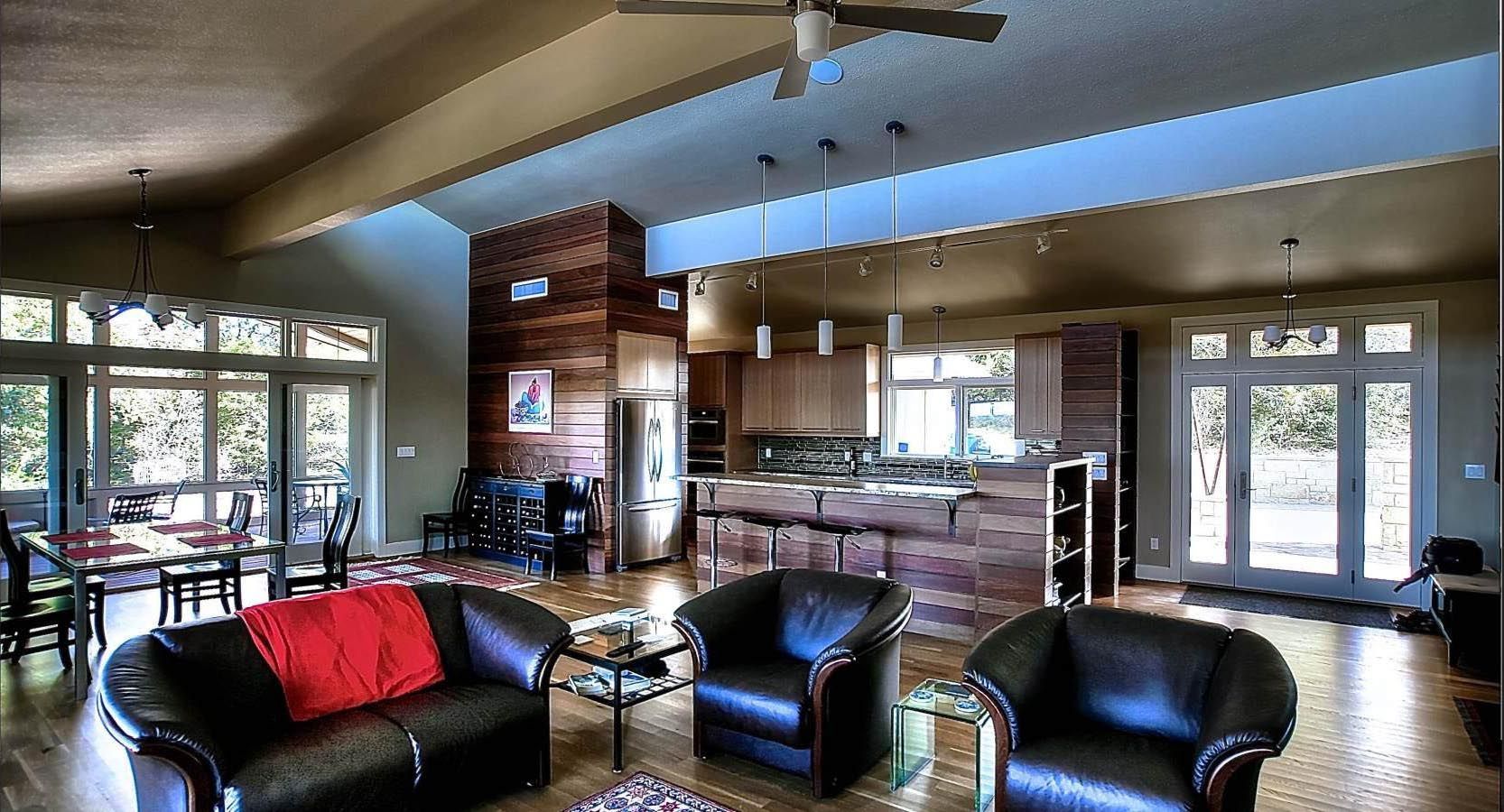 Spacious open-concept living area with dark leather furniture, a kitchen island, and large windows.