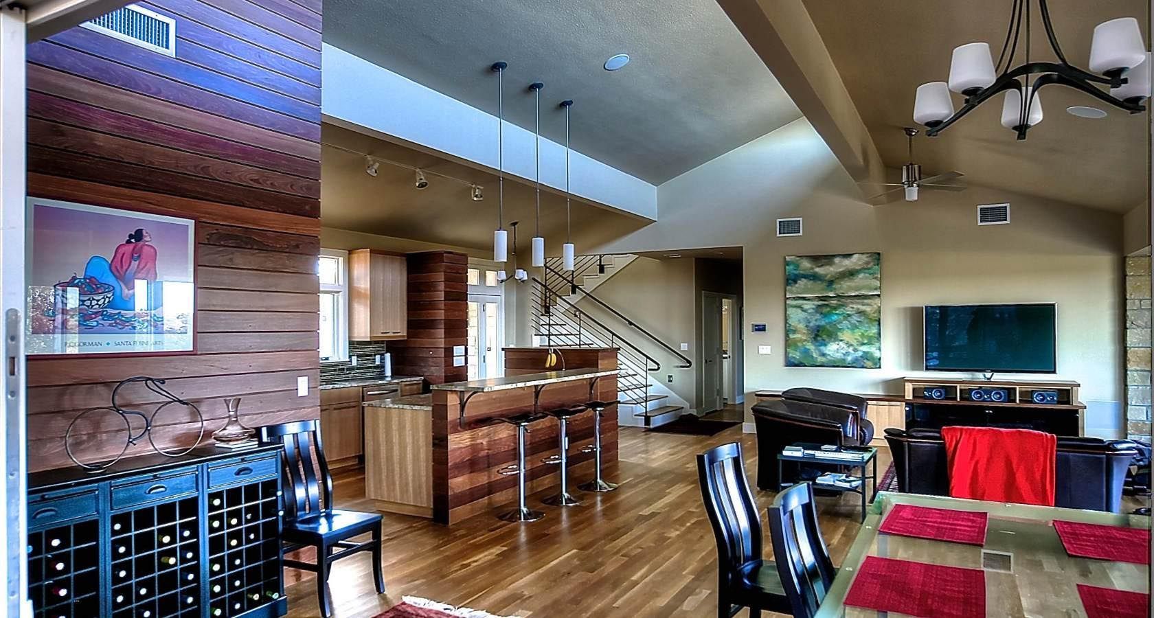 Spacious interior with kitchen, dining area, and living room. Wooden floors, a wine rack, and a staircase are visible.