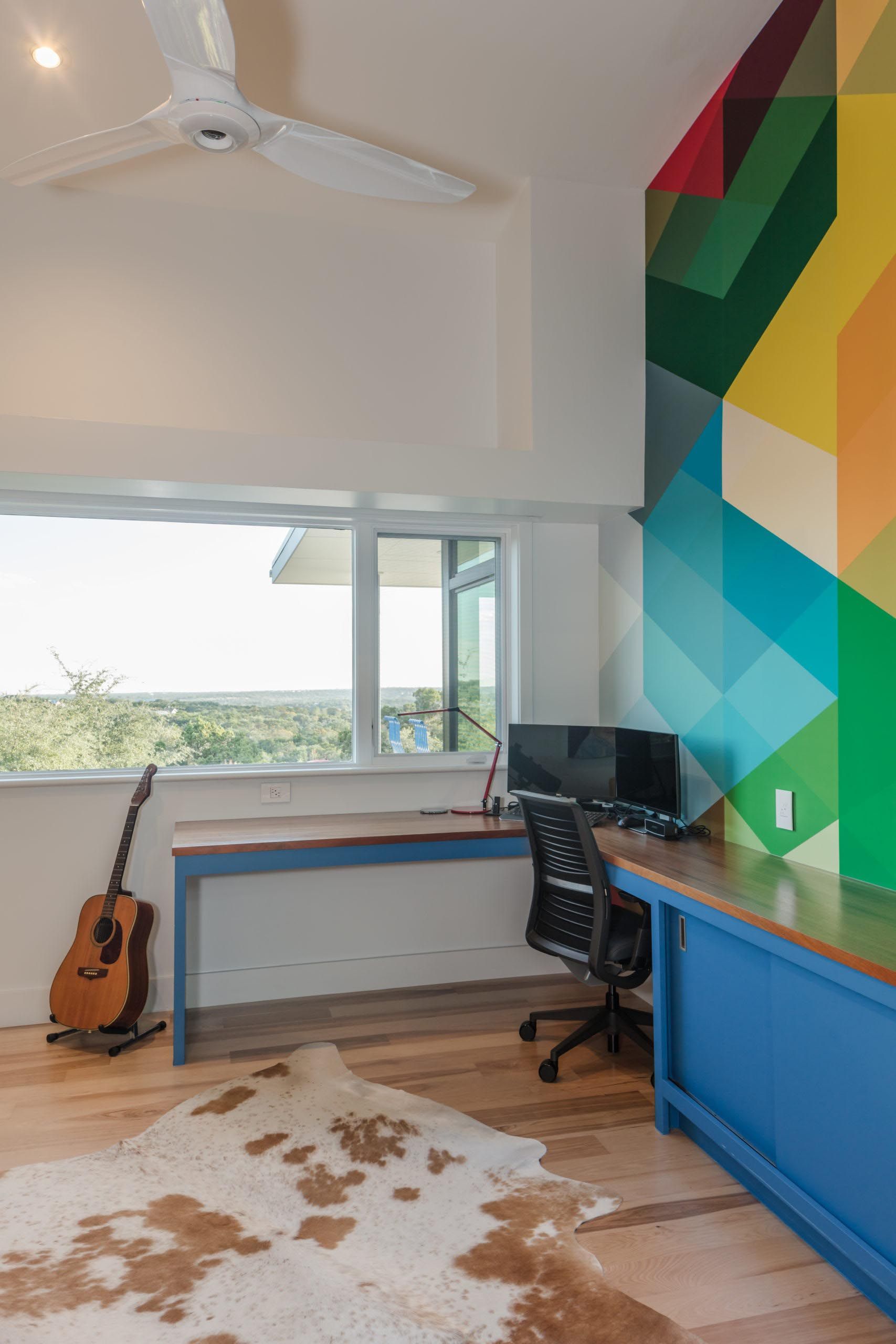 Office space with a blue desk, a geometric mural, guitar, and a cowhide rug.
