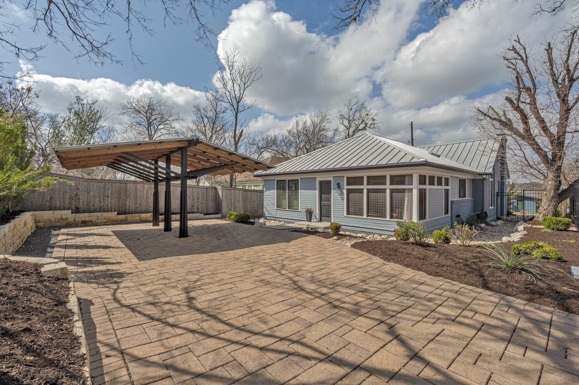 Blue house with a brick patio and a wooden pergola, under a cloudy sky.