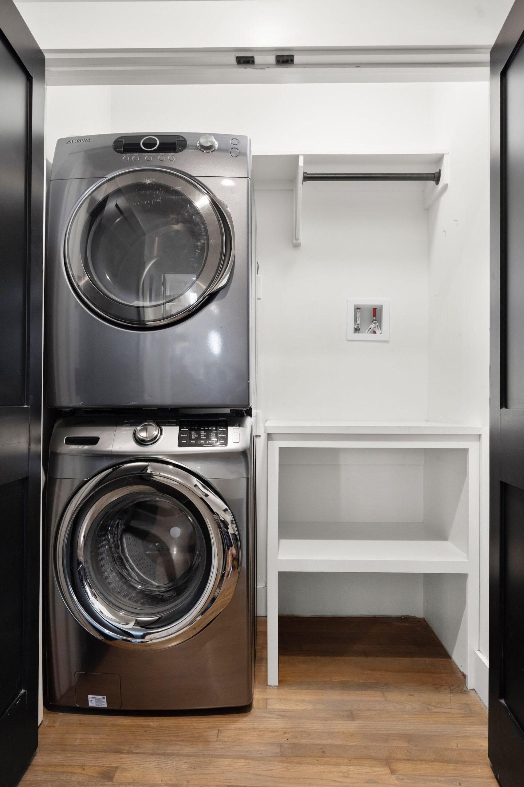 Stackable washer and dryer in a white laundry closet with shelves.