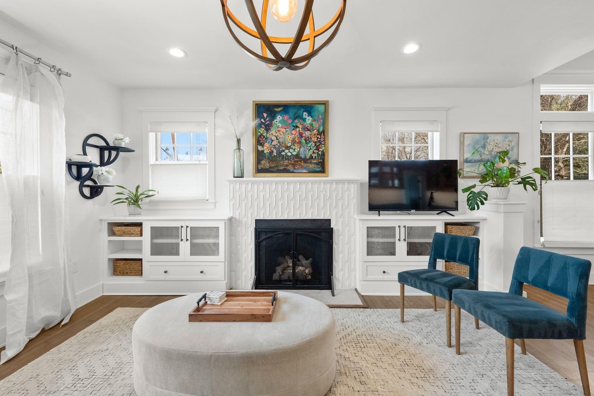 Living room with white walls, fireplace, blue chairs, and a round ottoman.