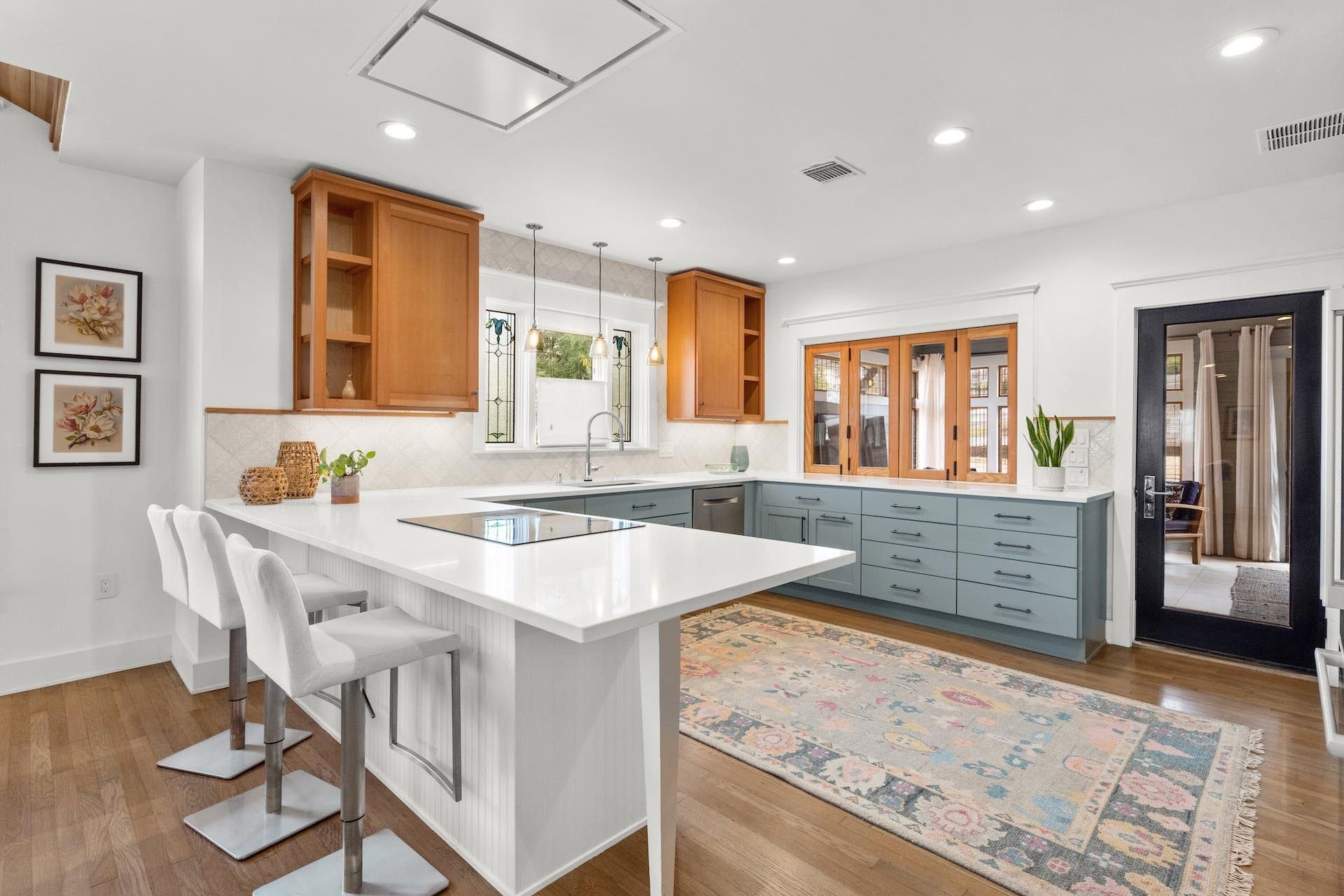 Modern kitchen with white countertops, blue cabinets, wood accents, and a bar with white stools.