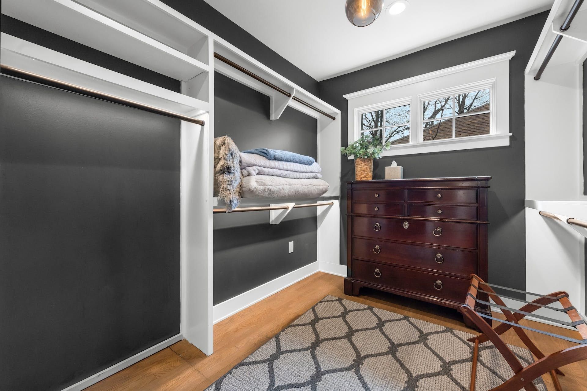 Walk-in closet with dark gray walls, white shelving, and a wooden dresser on a patterned rug.