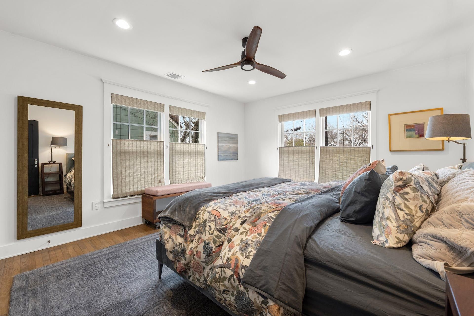 Bedroom with bed, mirror, windows, ceiling fan, and wooden floor.