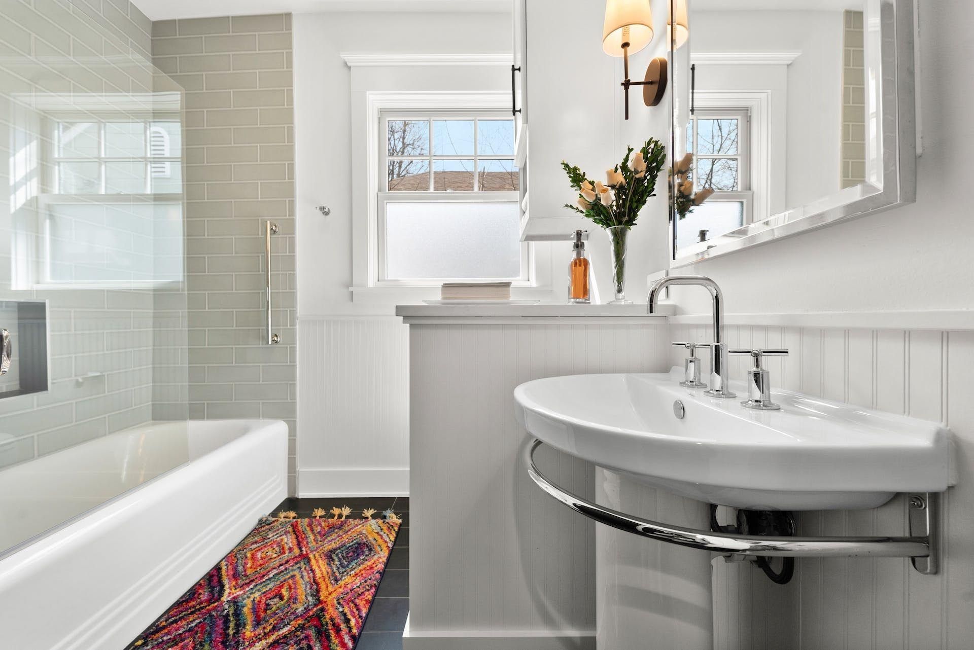 Bathroom with white walls, tub, sink, and a colorful rug.