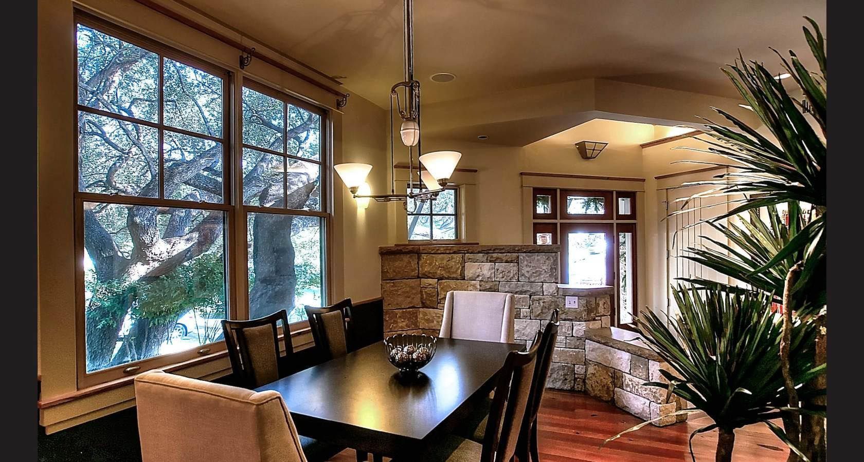 Dining room with dark wood table, chairs, large windows, stone wall, and chandelier.
