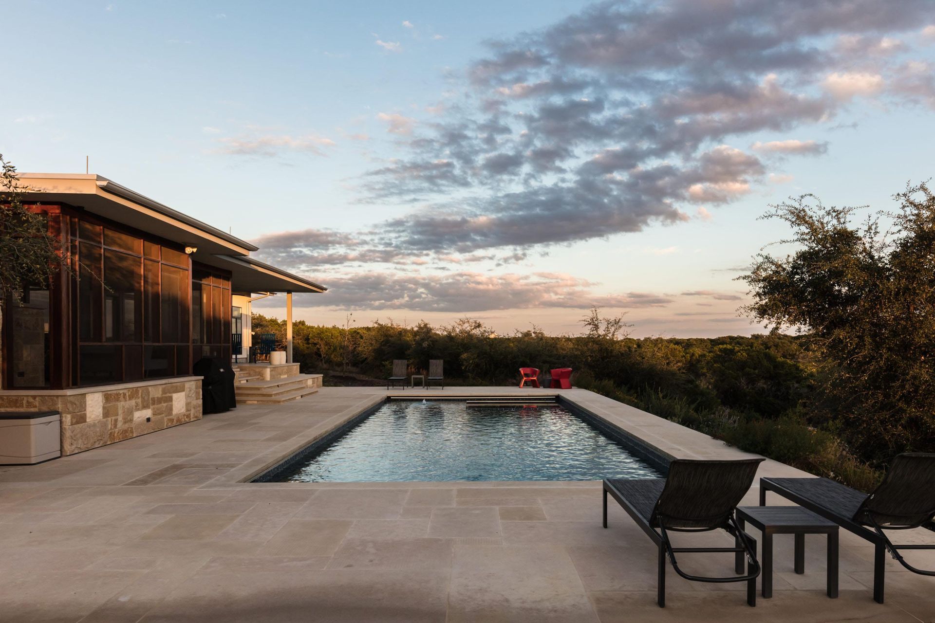 Poolside view with pool, loungers, house, and sunset sky.