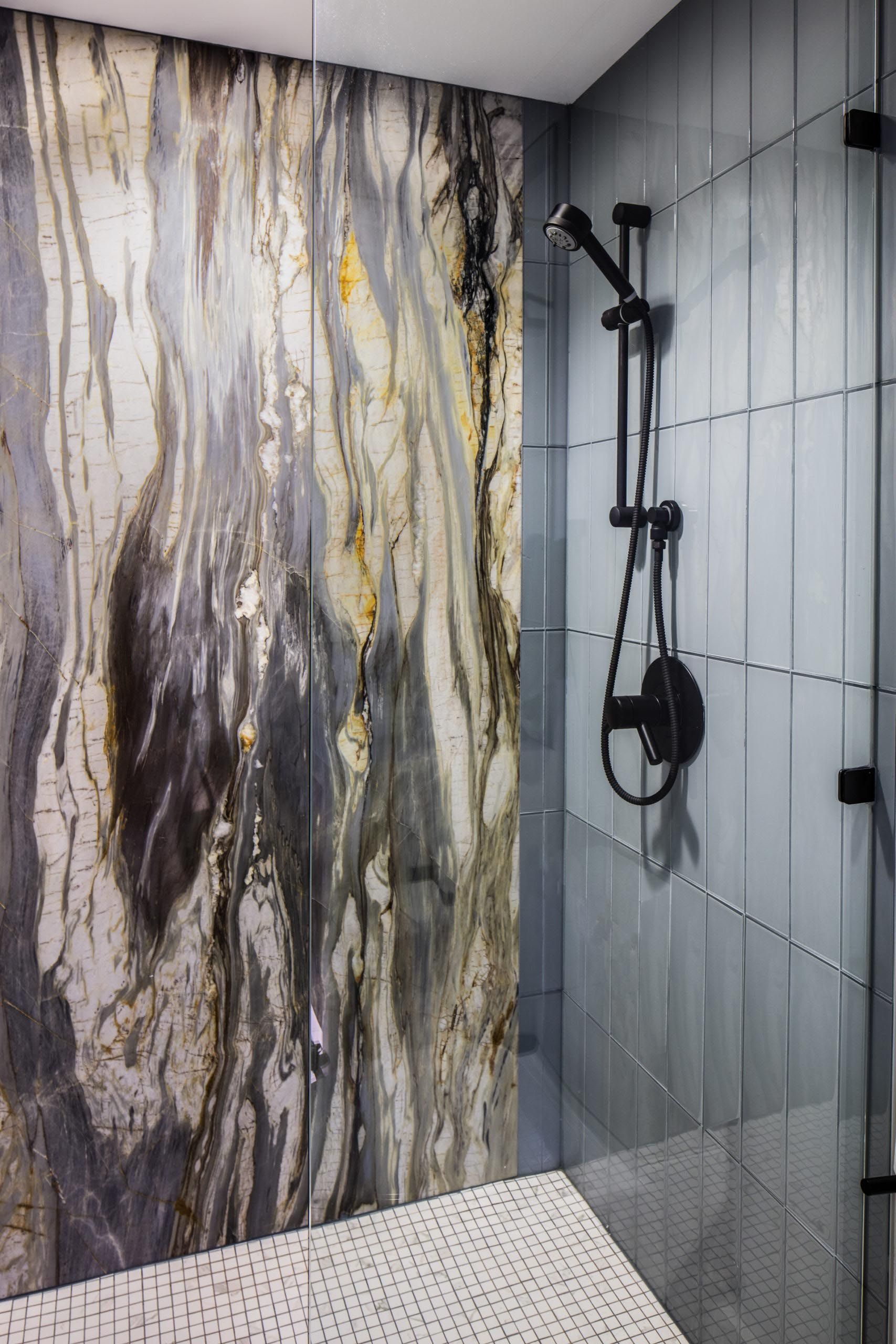 Shower with marble-patterned accent wall, vertical blue tile, black shower fixtures, and glass enclosure.