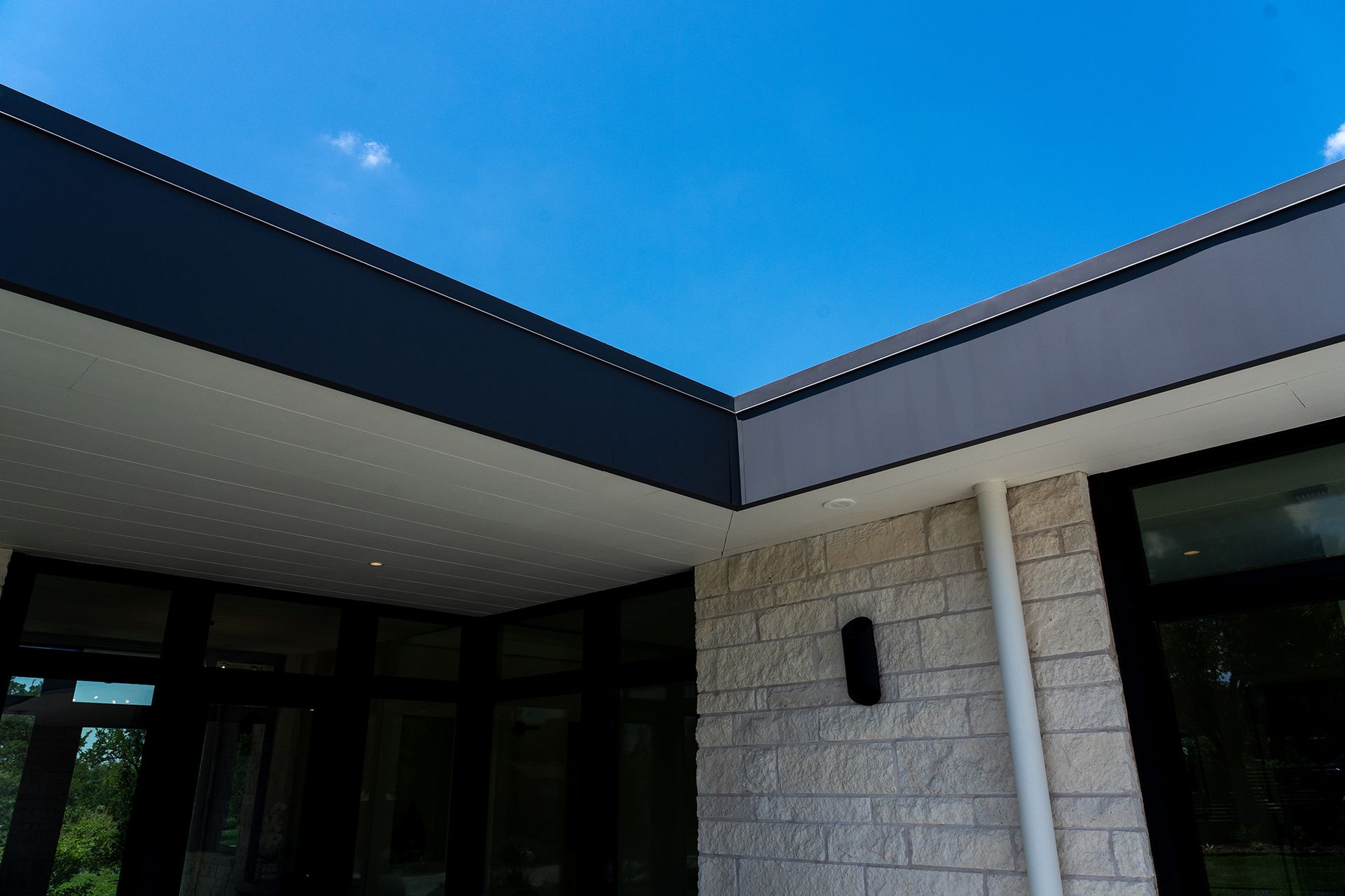Exterior corner of a modern building with dark gray trim, light brick, and a bright blue sky.