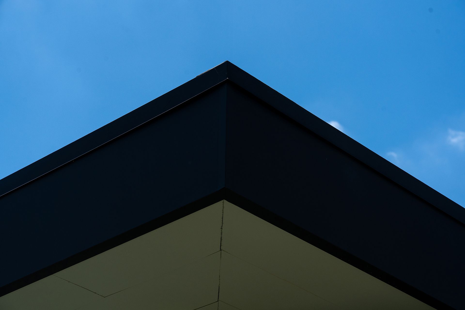 Dark roof corner against a blue sky; beige underside.