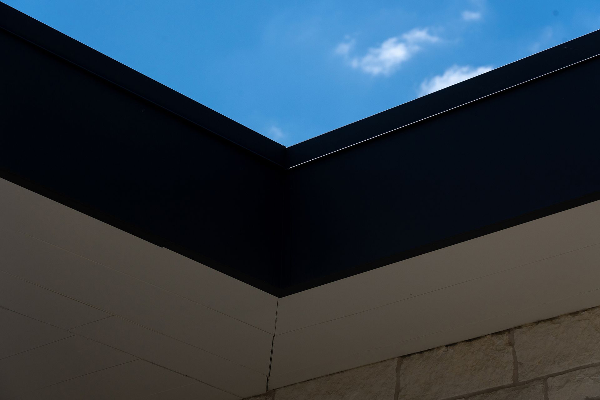 Black roof edge against a blue sky, with white and stone-colored walls.