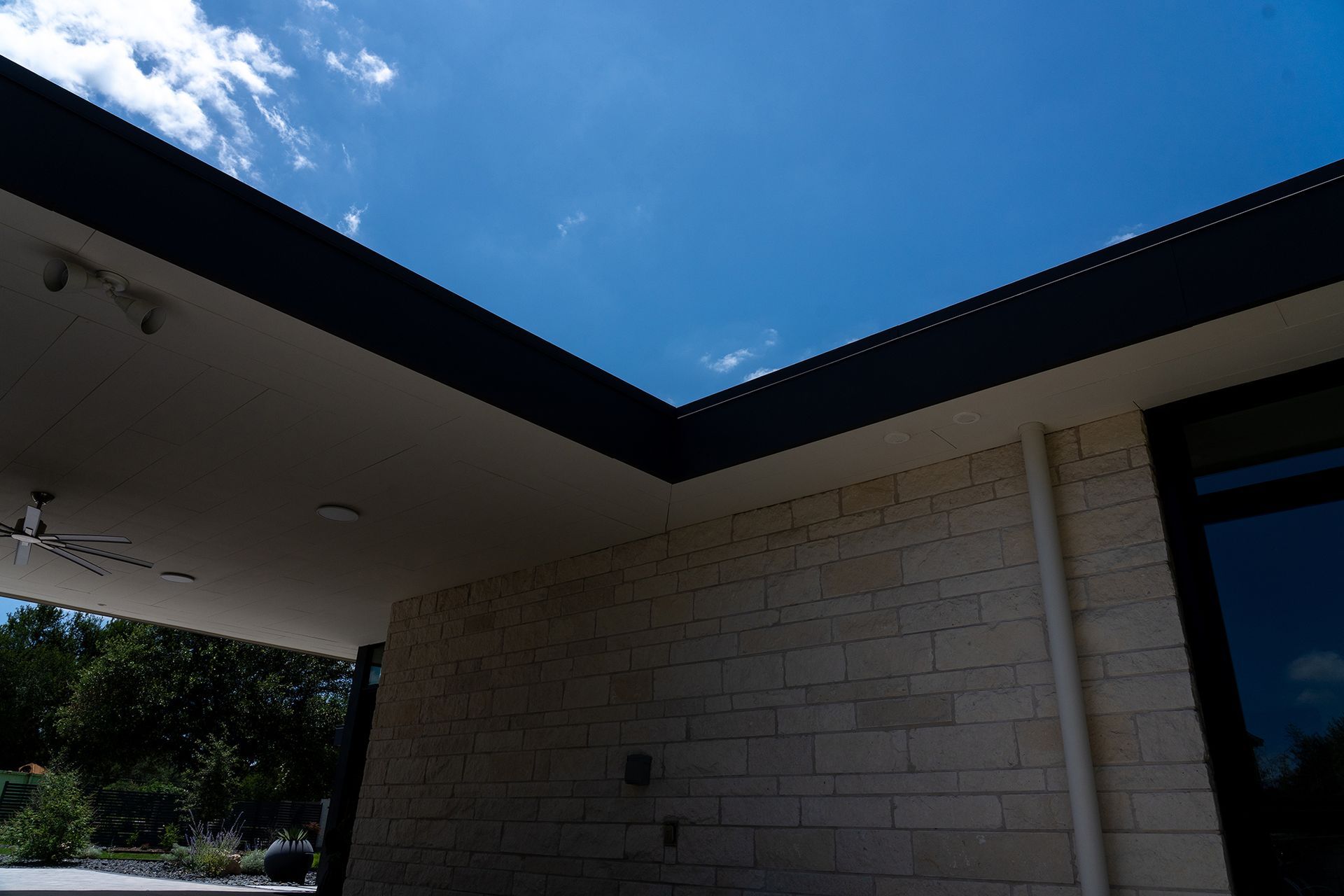 Exterior of a modern building with a black roof and light-colored brick walls, under a blue sky.
