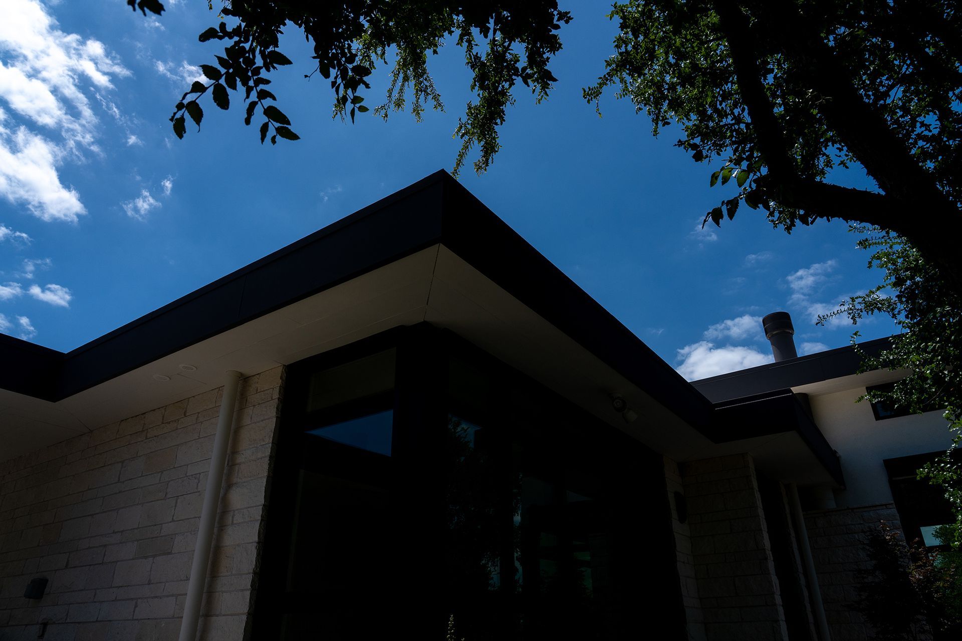 A modern house with a dark roof and large windows against a blue sky with clouds.