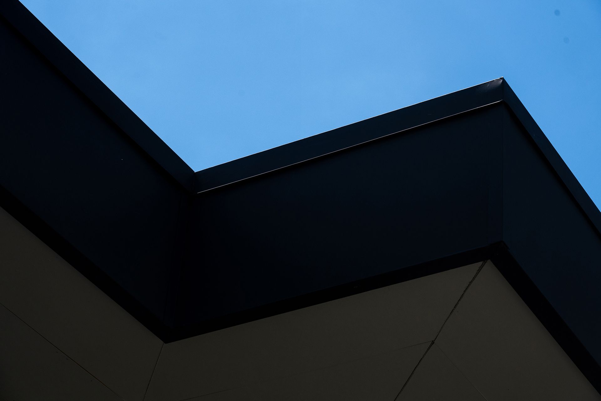 Dark roof corner against a clear blue sky, with visible gutter detailing and white exterior wall.