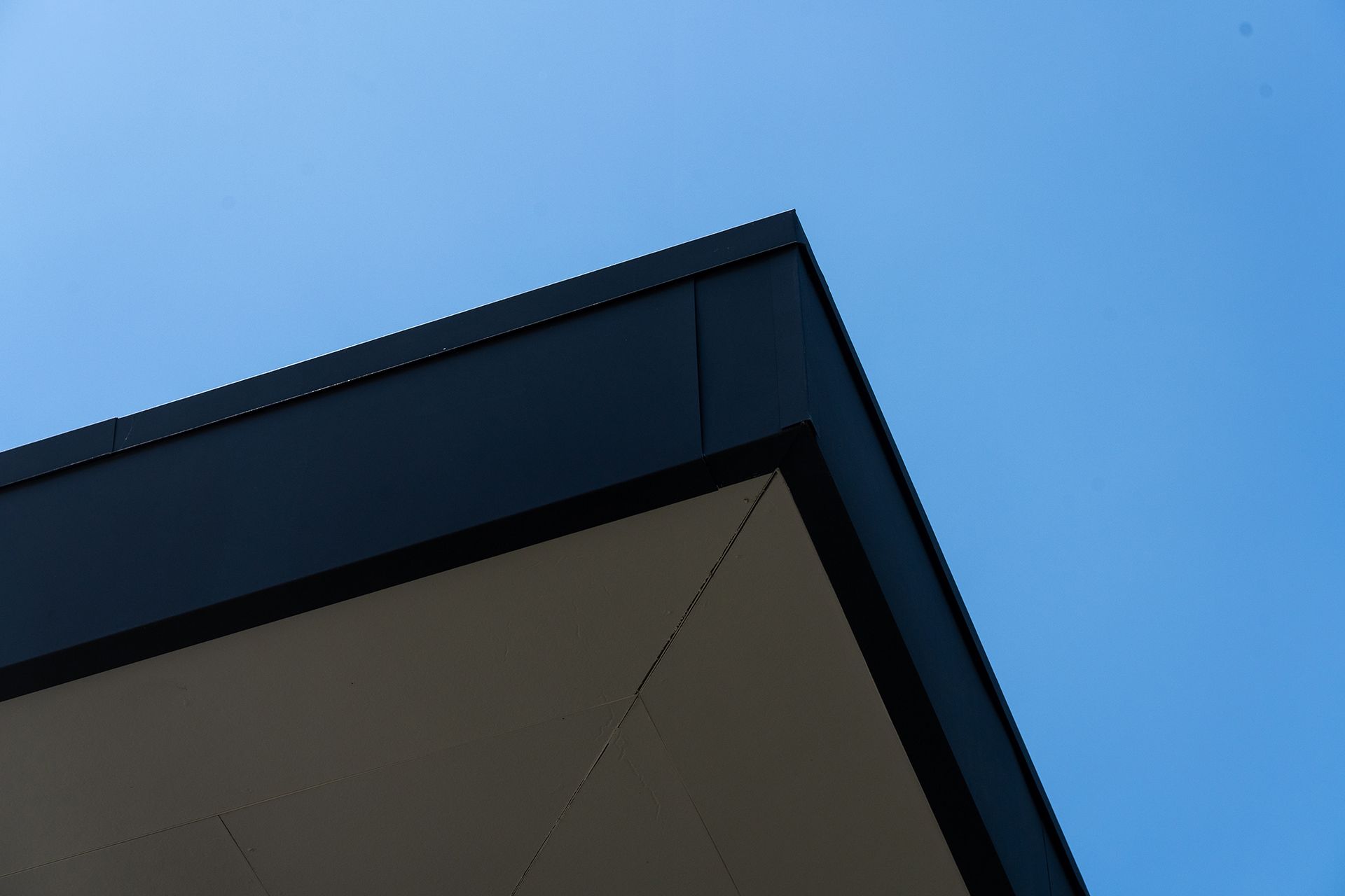 Corner of a dark building roof against a bright blue sky.