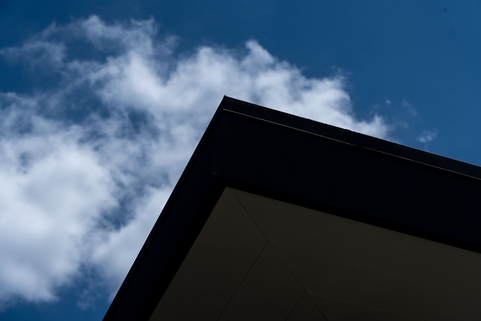 Corner of a dark building against a bright blue sky with fluffy white clouds.