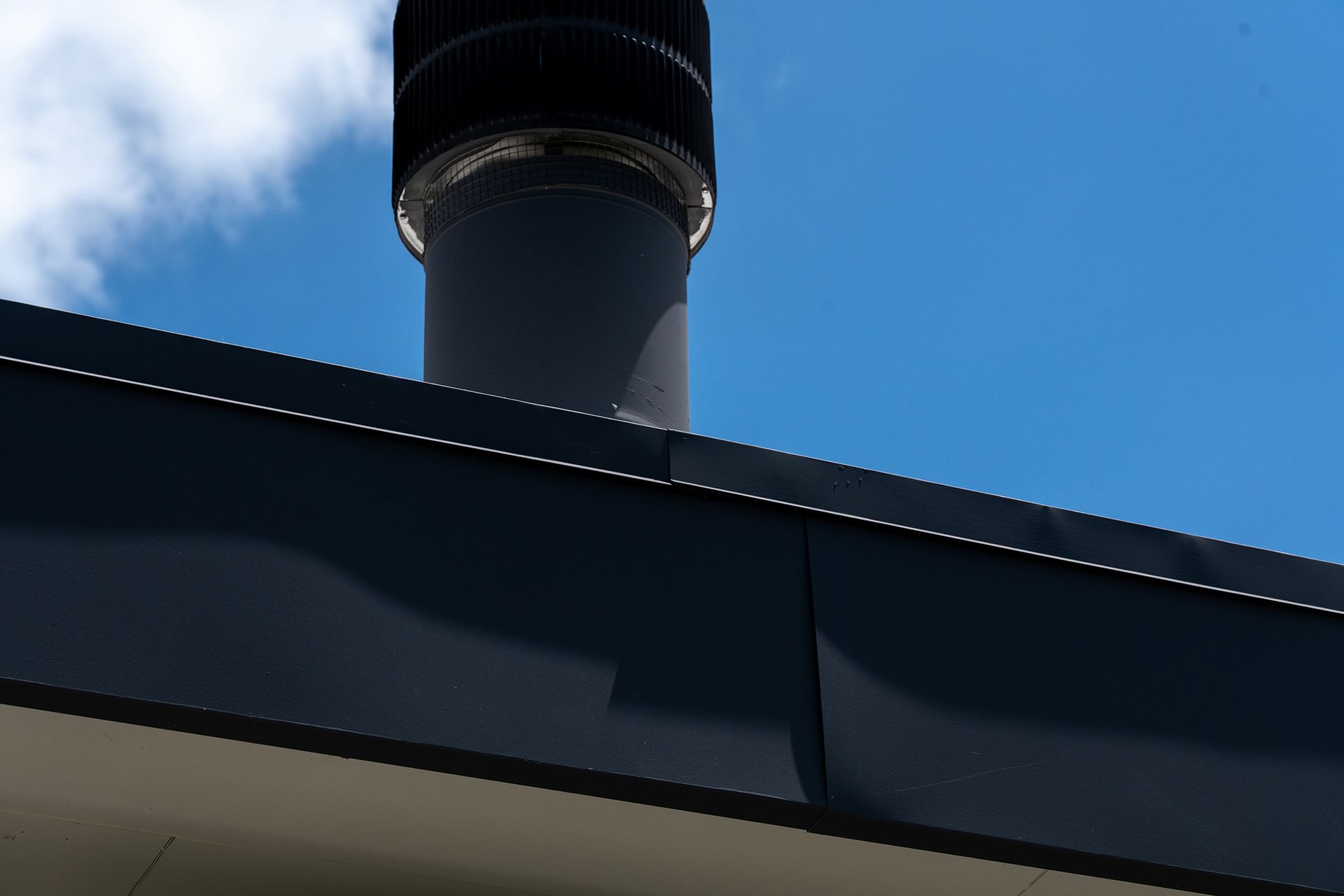 Black chimney pipe against blue sky, extending from a dark roof.