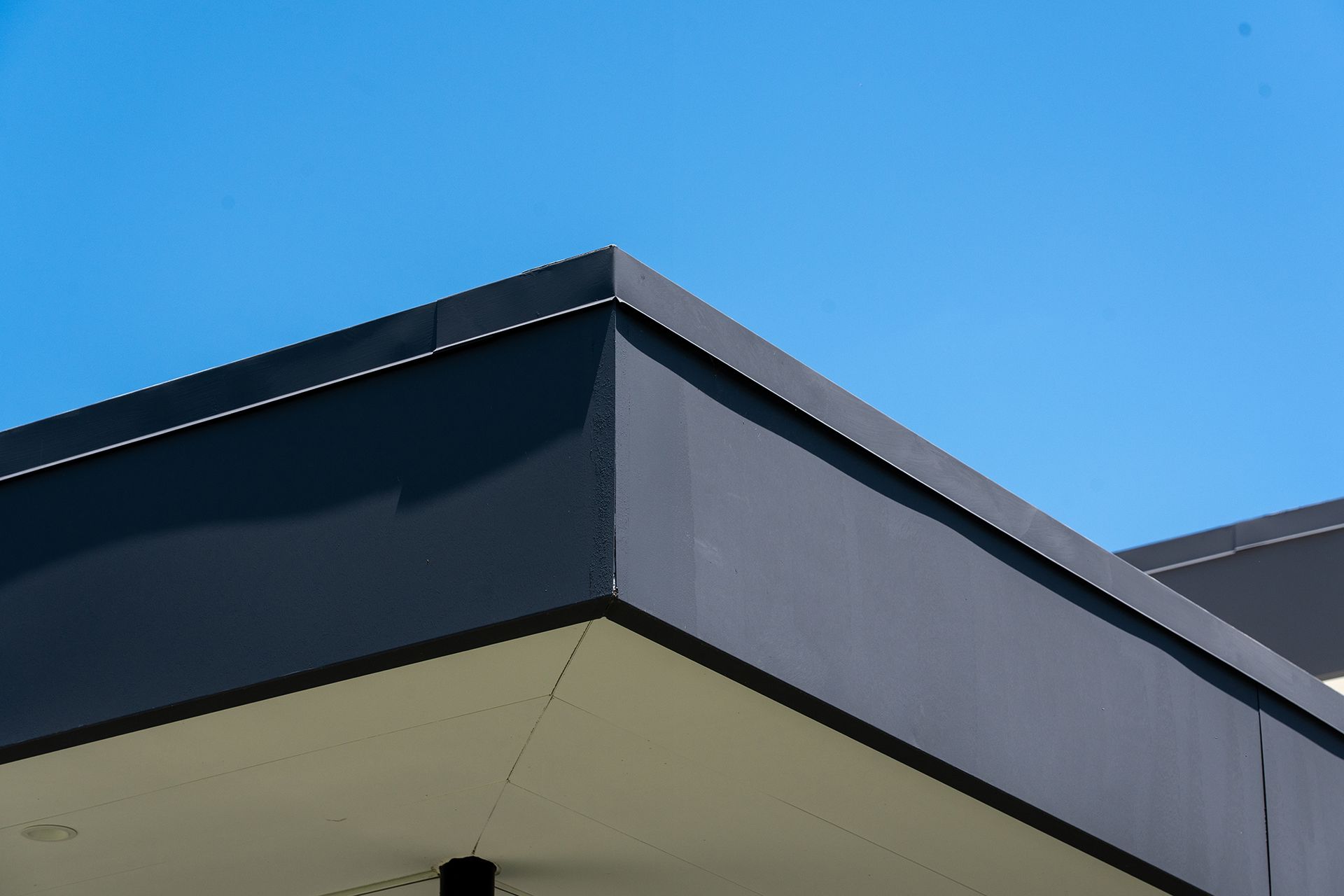 Black building corner against a clear blue sky.