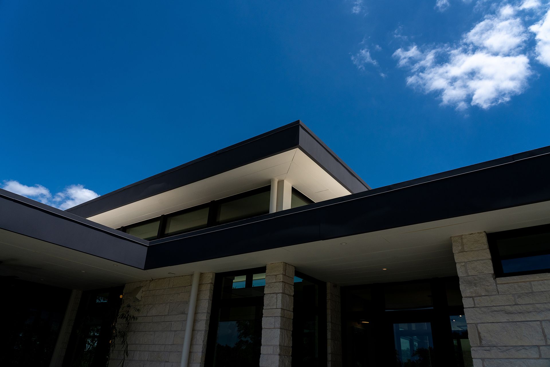 Modern building with dark roof against a bright blue sky with wispy clouds.