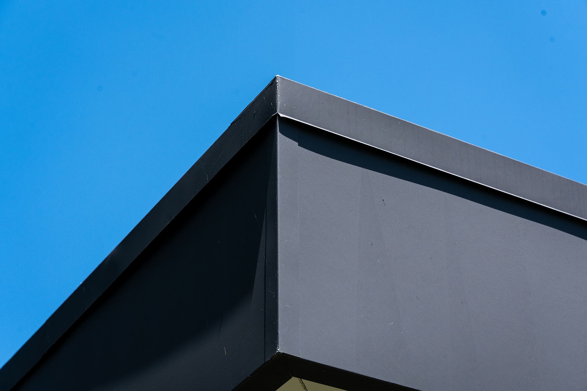 Close-up of a modern building's dark gray corner against a blue sky.