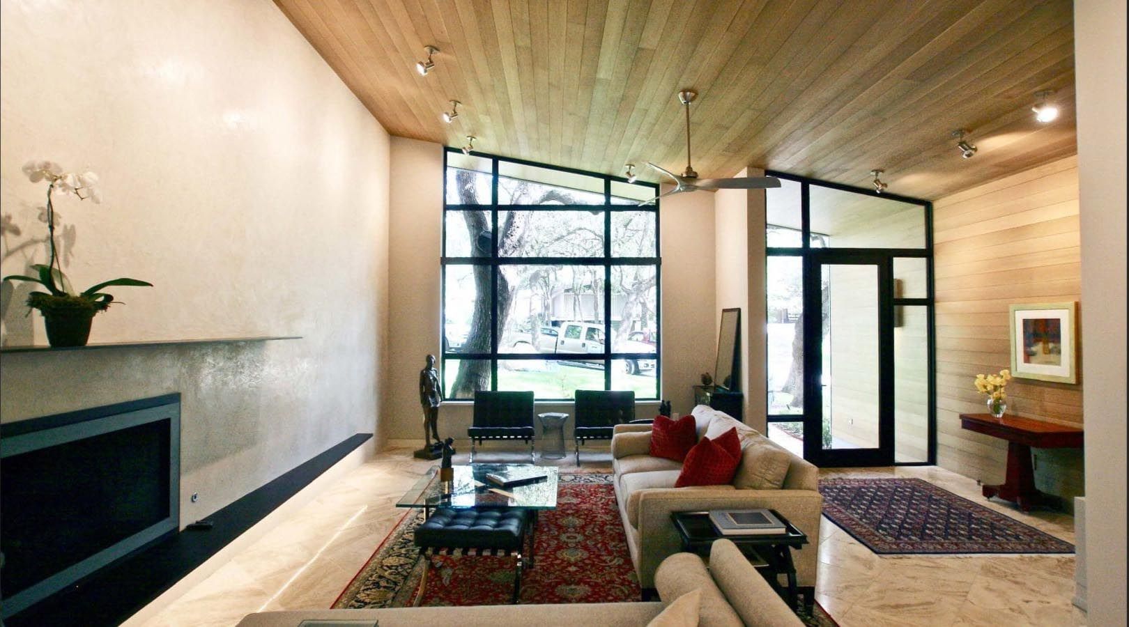 Modern living room with wood ceiling, large window, fireplace, and red rug.