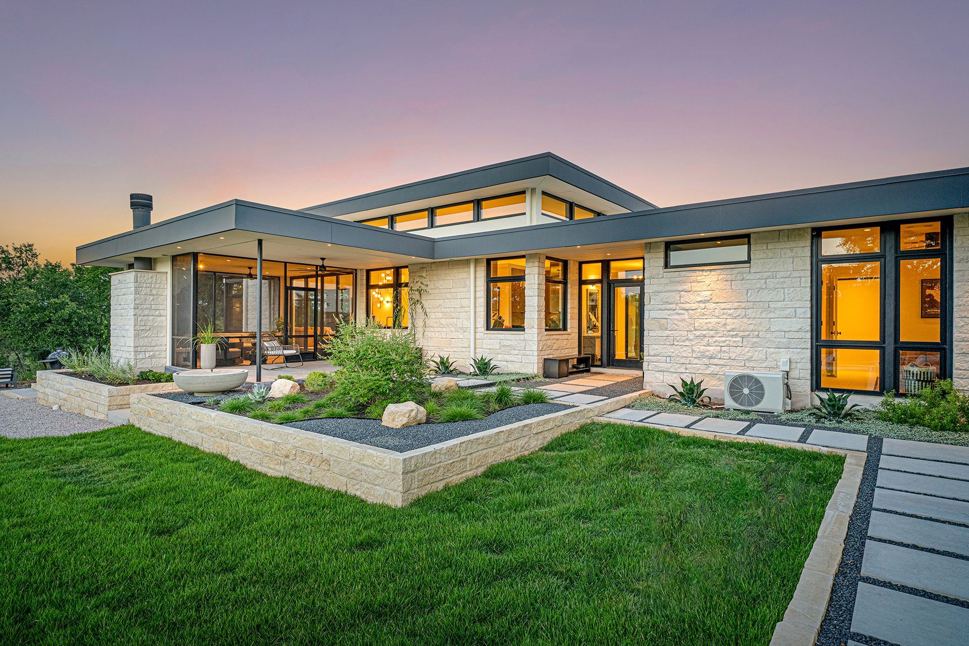 Modern home exterior with stone facade, dark trim, and landscaped yard.