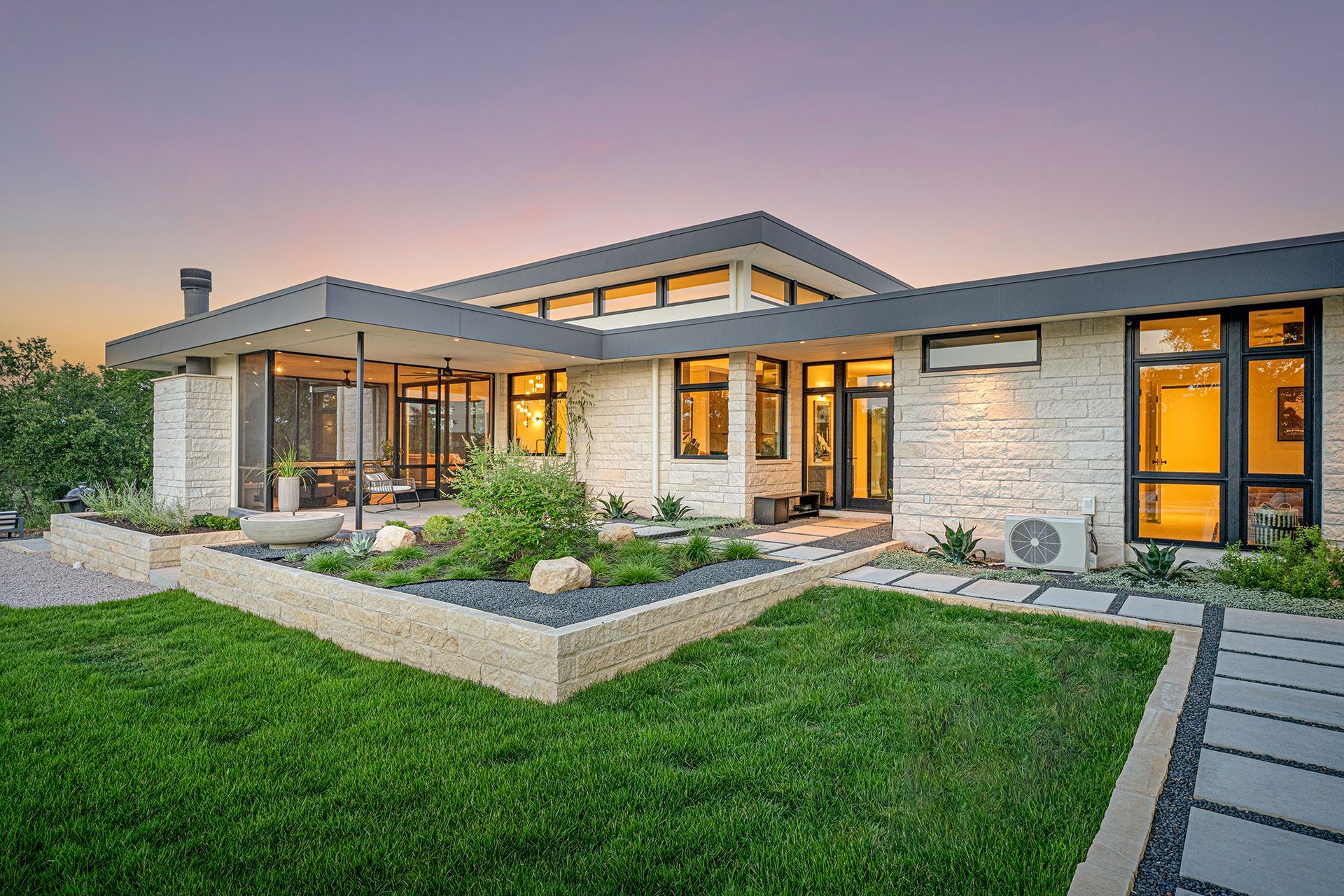 Modern house exterior with stone facade, dark trim, and landscaped yard at dusk.