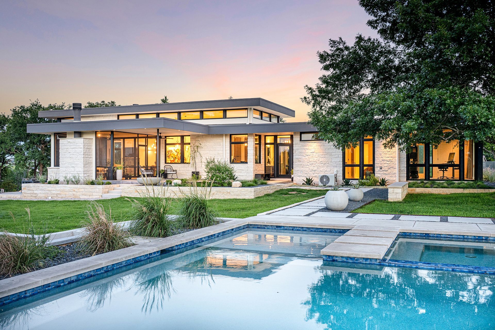 Modern home with pool; stone exterior, glass windows, grassy lawn.