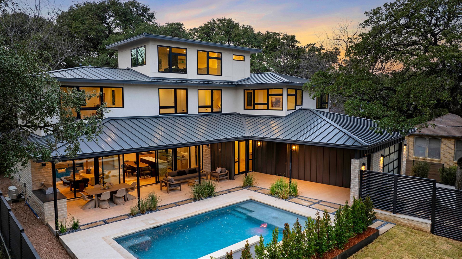 Modern two-story house with a pool in the backyard, surrounded by trees.