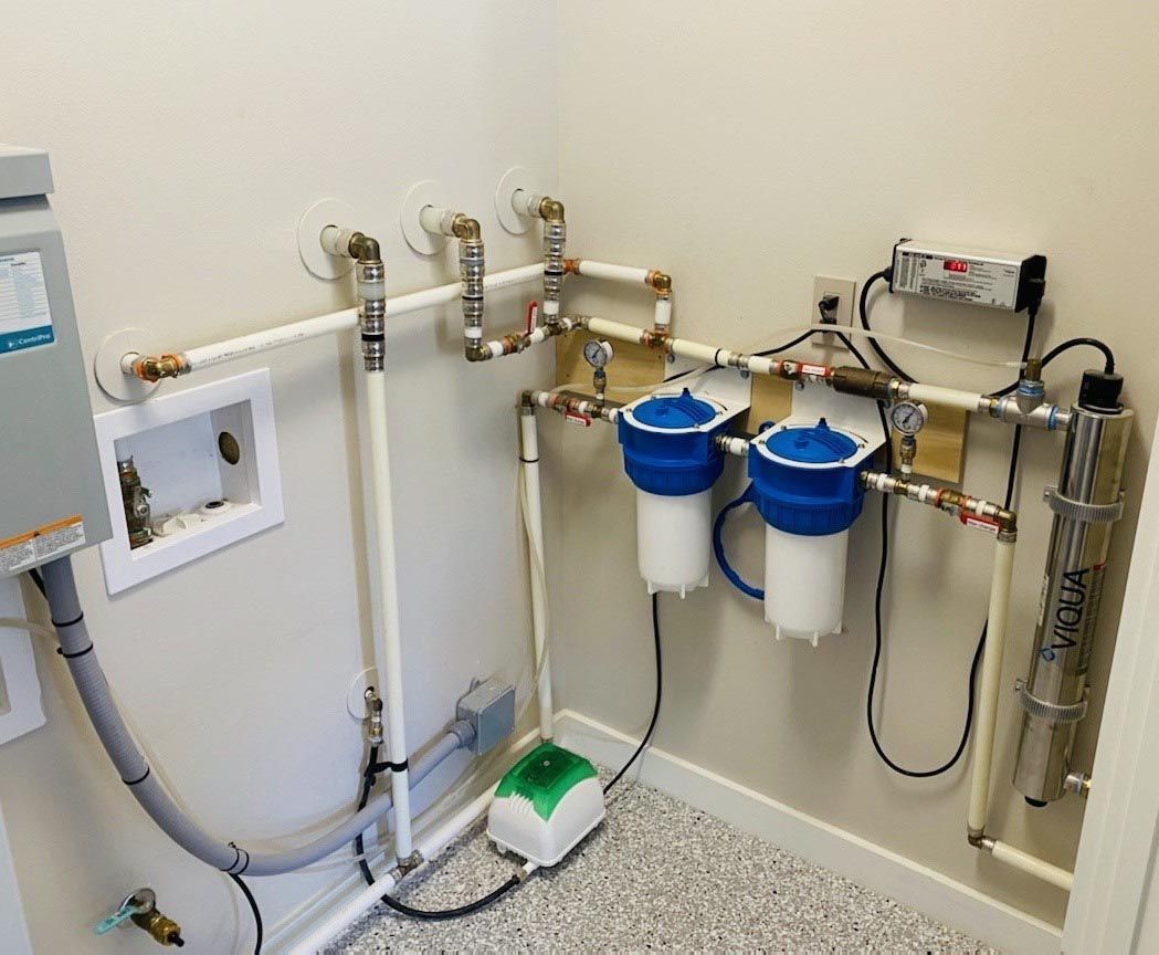 Water filtration system with various pipes, filters, and a water heater, installed against a wall in a utility room.