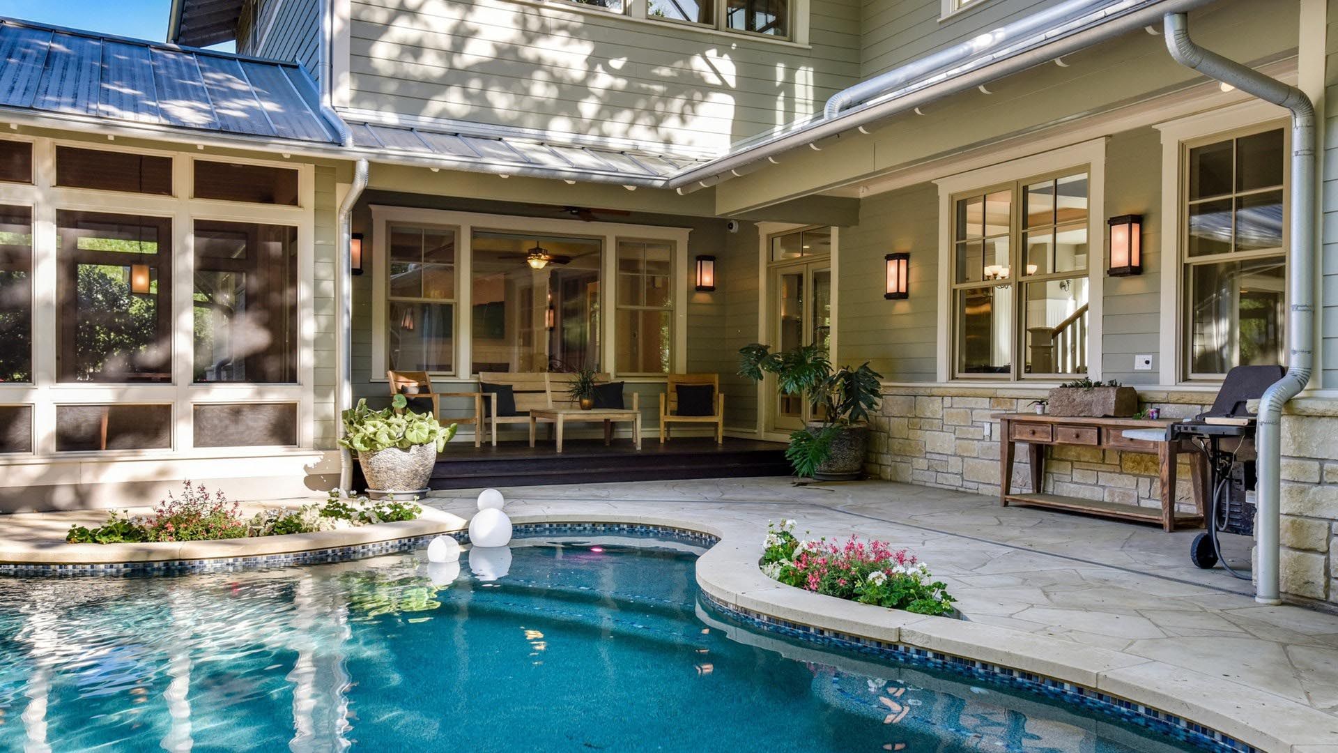 Backyard patio with pool, house, and screening. Teal water reflects sunlight.