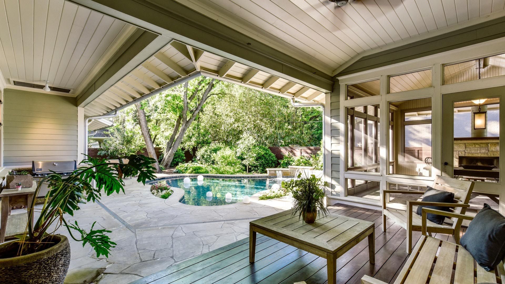 Covered patio overlooking a pool and lush greenery. White wood furniture. Bright, sunny day.