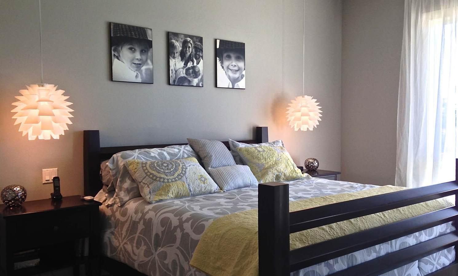Bedroom with gray walls, black bed, white bedding, yellow accents, and three black and white photos above the bed.