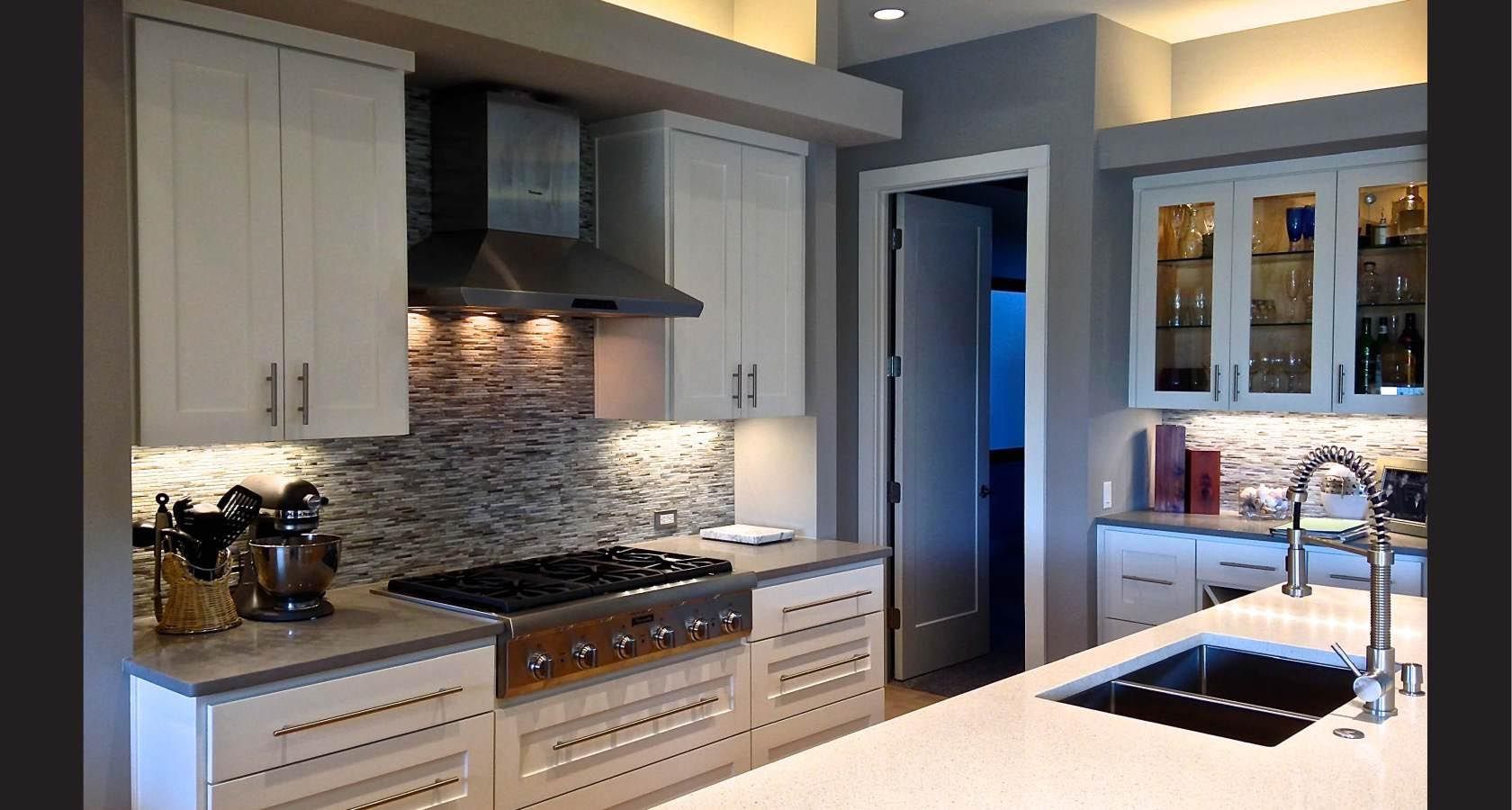 Modern kitchen with white cabinets, stainless steel range hood, and tile backsplash.