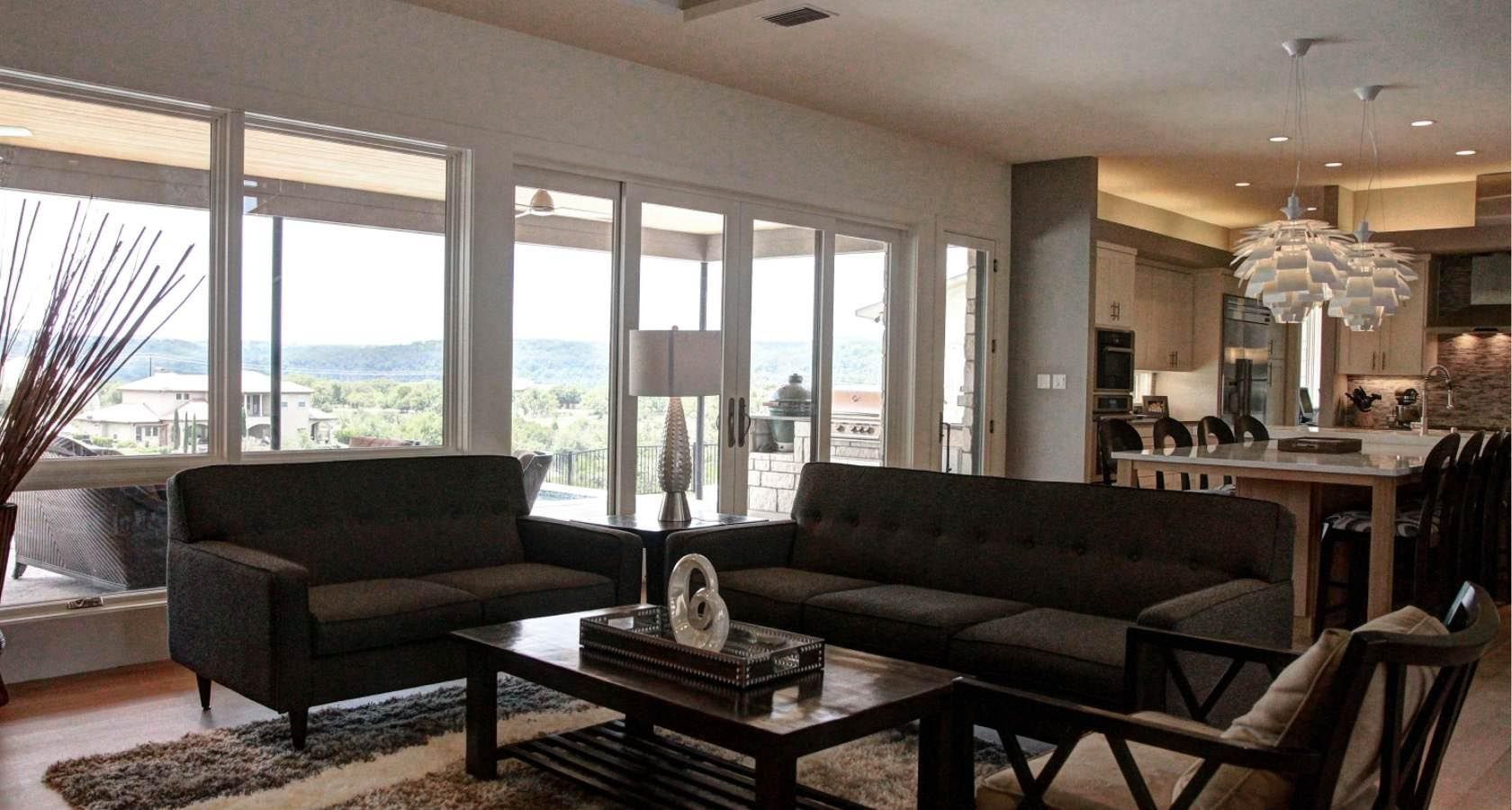 Living room with dark gray furniture, large windows, and an open kitchen.