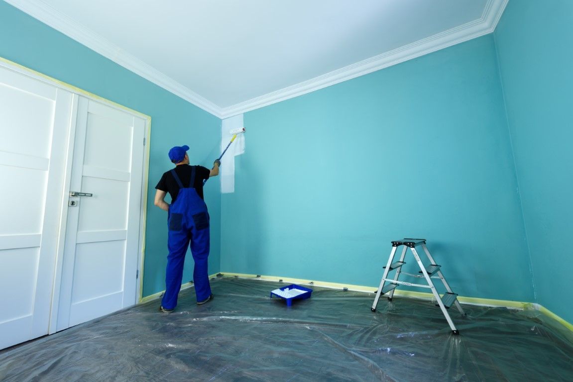Painter painting a light blue room near a ladder and open paint tray