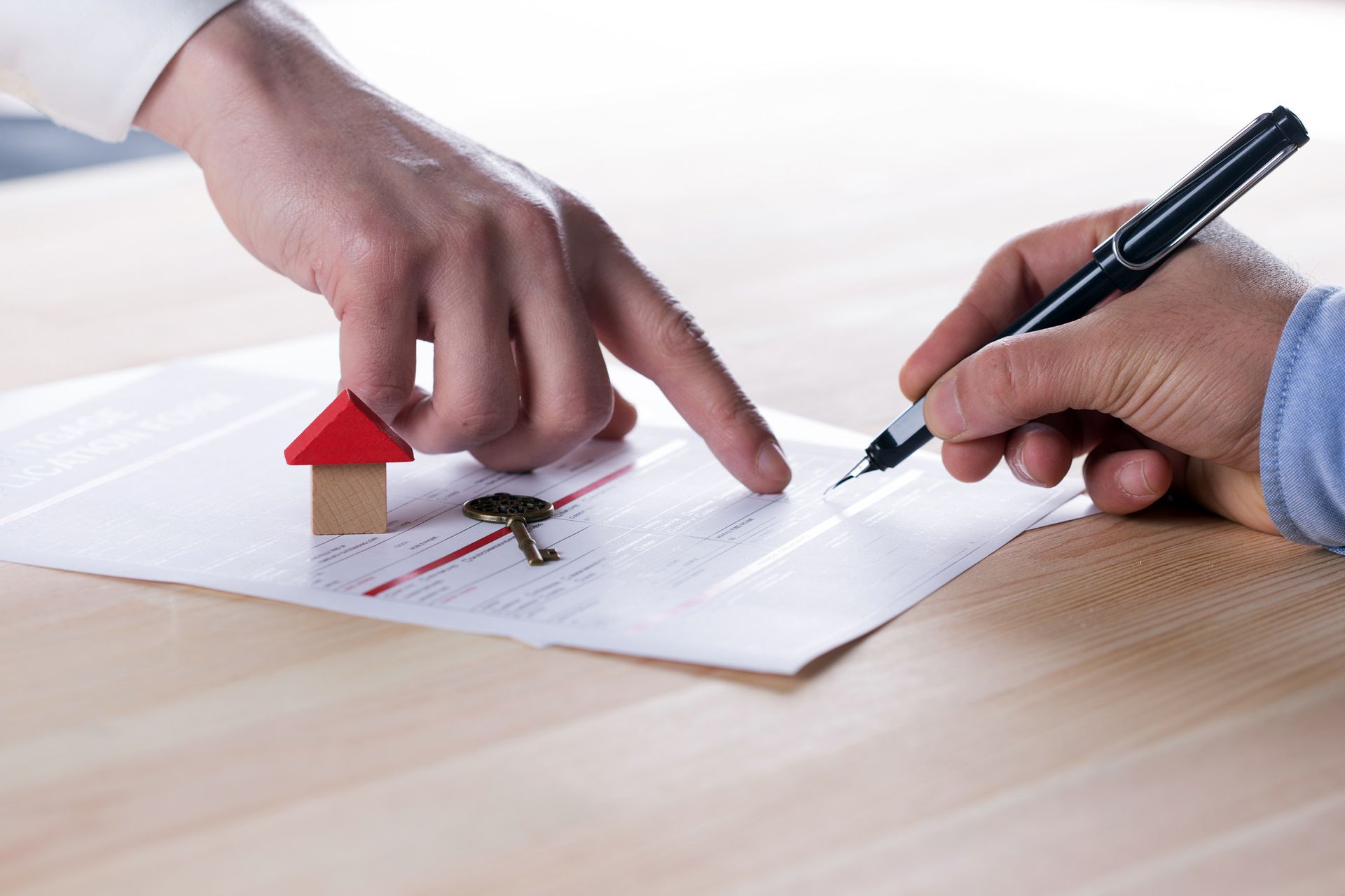 a person is signing a document with a small house and keys on it .