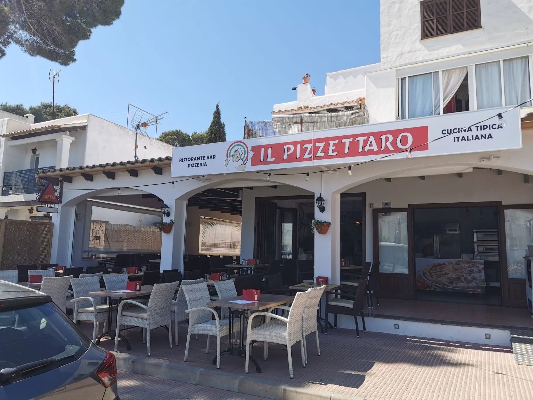 Tavoli all'aperto presso il ristorante Il Pizzattaro con tavoli e sedie bianchi sotto un cielo azzurro e soleggiato.