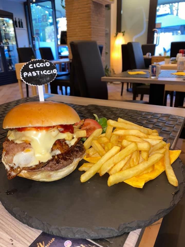 Hamburger e patatine fritte su un piatto. A guarnire l'hamburger, formaggio fuso e uno stuzzicadenti.