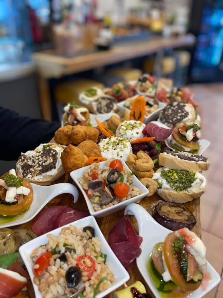 Un vassoio di legno traboccante di antipasti assortiti, tra cui bruschette, arancini e insalate.