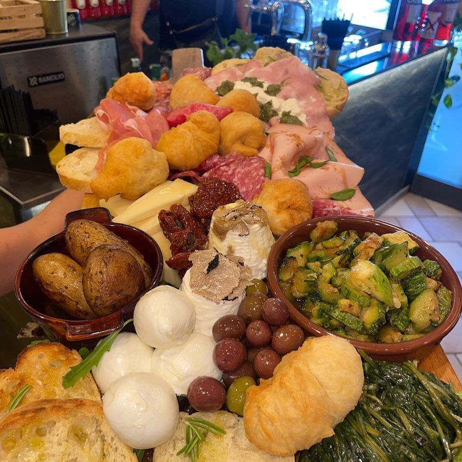 Tagliere di legno con vari cibi italiani: salumi, formaggi, olive, pasta fritta e verdure arrostite.