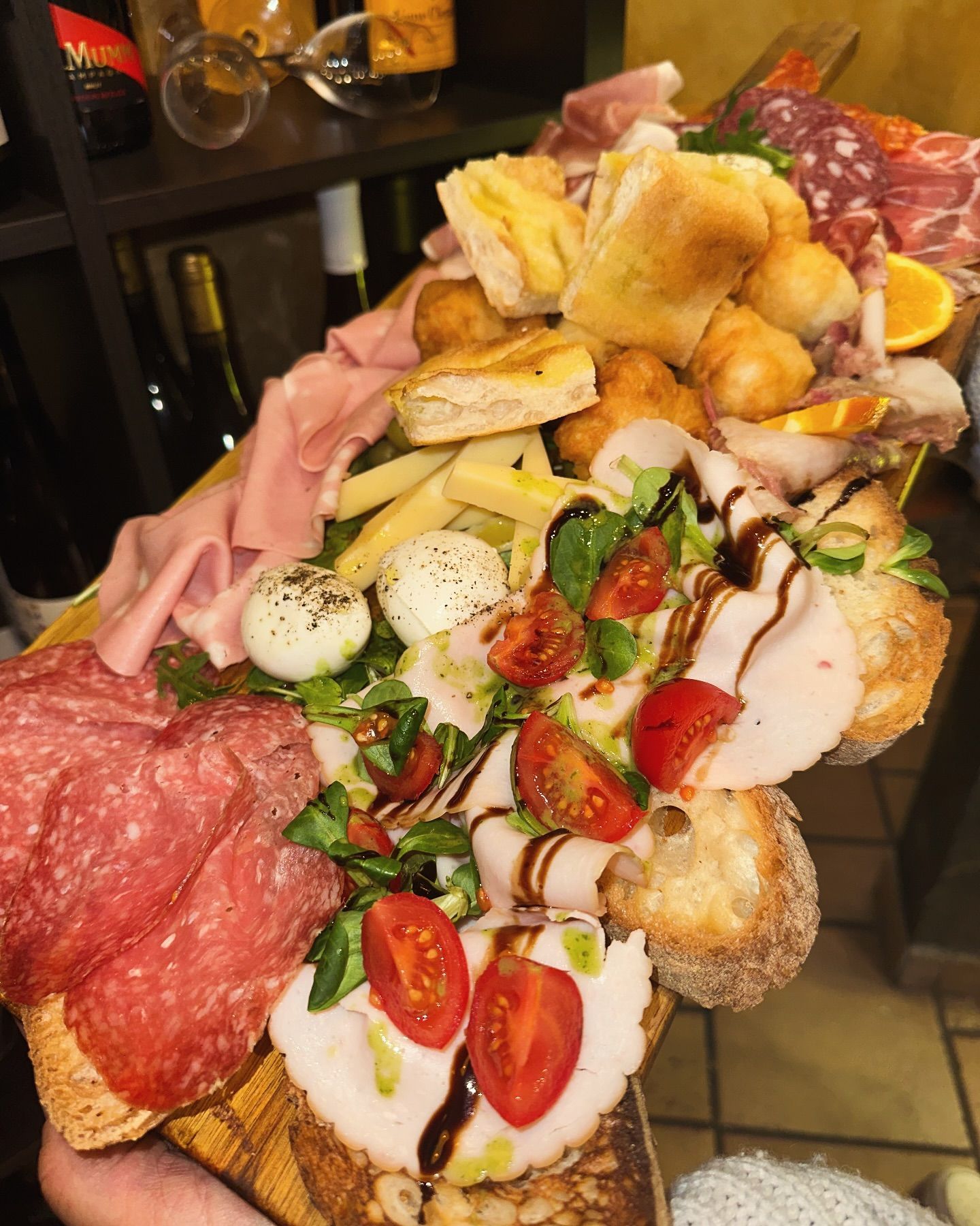 Tagliere di salumi: salame, prosciutto, formaggio, pomodori, pane e palline di pasta fritte, su un vassoio di legno.