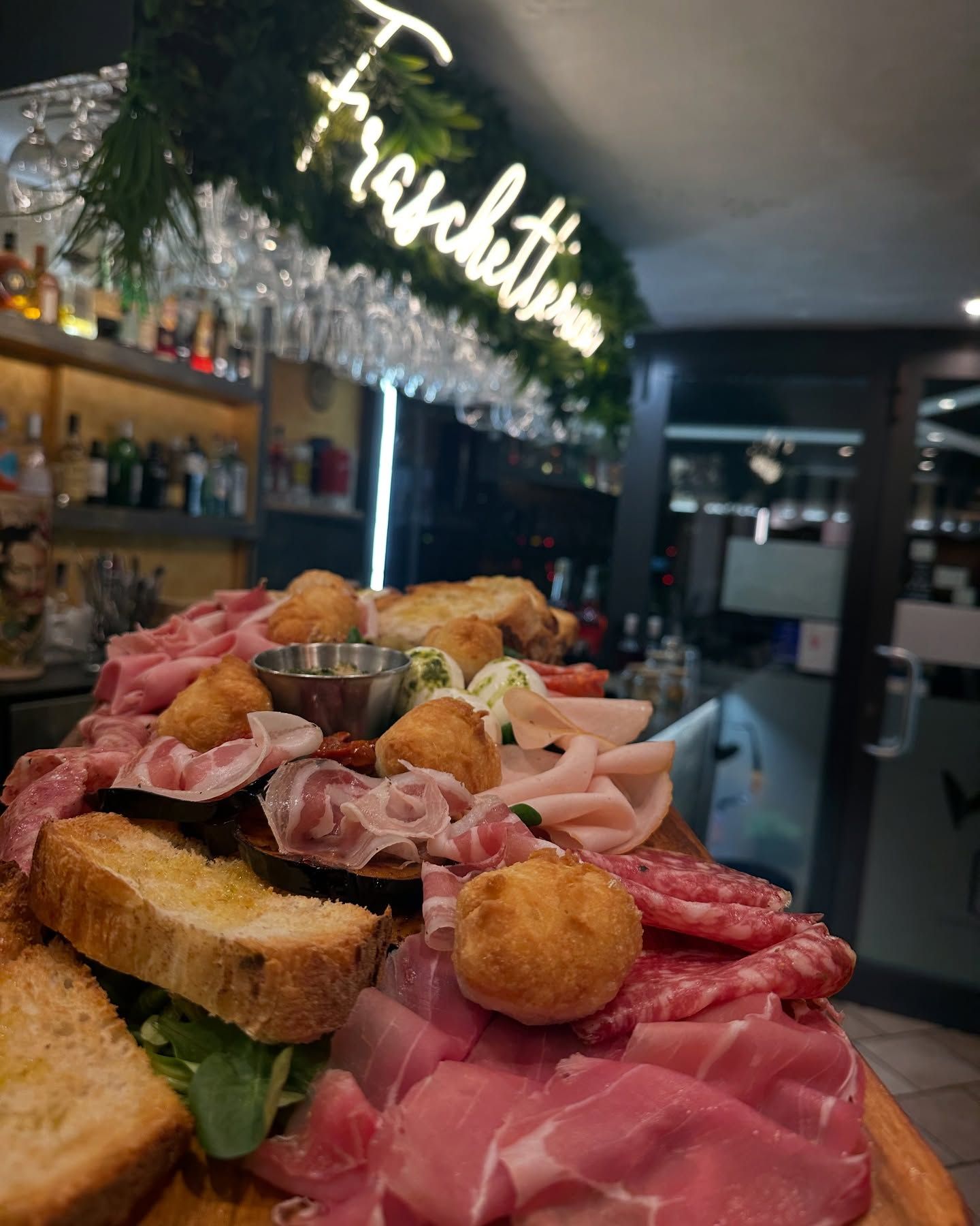 Tagliere di salumi, formaggi e polpette fritte, sotto l'insegna al neon